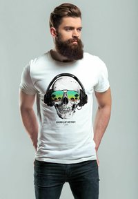 Ein weißes Baumwoll-T-Shirt mit einem Grafikaufdruck eines Schädels, der Kopfhörer und Sonnenbrille trägt, mit Reflexionen von Palmen. Darunter steht der Text "SOUNDS OF DETROIT".