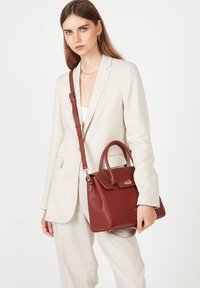 Borsa a mano in pelle rossa con forma strutturata, manici superiori e una tracolla removibile. Presenta una chiusura a soffietto e sottili dettagli in oro.