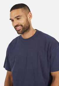 T-shirt en coton bleu marine avec une coupe décontractée, un col rond et des manches courtes. Texture lisse avec des détails de couture minimaux.