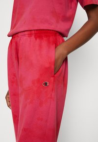 Rød tie-dye sweats med elastisk talje og sidelommer. Har et lille broderet logo på venstre hofte. Blødt bomuldsstof.