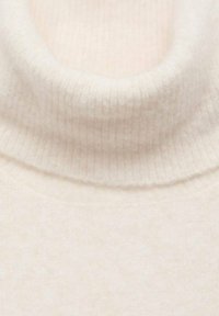 Rebrast pulover s turtleneck ohlapnem iz mehkega bež materiala, ki se prilega in ima gladko teksturo. Ni opaznih vzorcev ali kovinskih detajlov.