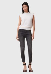 Top de punto sin mangas de color blanco con un bajo acanalado corto, combinado con unos jeans ajustados gris oscuro con bajos deshilachados y sandalias de tiras negras.