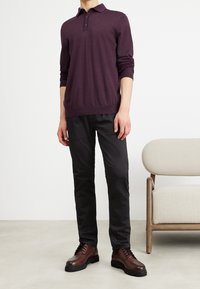 Dunkellila Langarm-Polohemd mit Kragen und drei Knöpfen, kombiniert mit schwarzen Slim-Fit-Hosen und braunen Schnürschuhen.