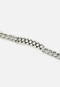 Pulseira de corrente prateada com elos alternados entre grossos e finos. Apresenta uma secção texturizada com um padrão quadrado e acabamento polido.