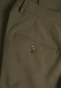 Pantalones verde oliva de tejido texturizado con parte delantera plana, que cuentan con un bolsillo trasero asegurado por un botón circular.