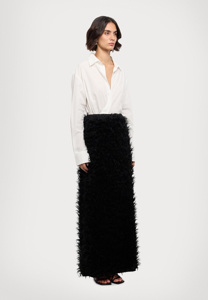 Chemise blanche à boutons avec un décolleté en V profond, associée à une longue jupe noire en plumes. La jupe a une texture avec une apparence duveteuse et en couches.