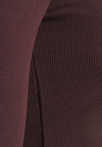 Close-up de tecido canelado em um profundo borgonha. A textura é suave, com linhas verticais que destacam um design justo e ajustado.