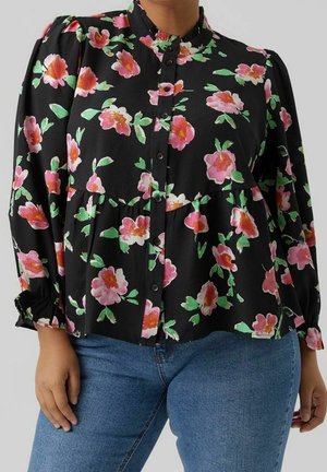 Personne portant un chemisier noir boutonné sur le devant, à imprimé floral rose et à taille froncée, associé à un jean bleu.