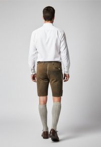 Hnědé kraťasy se bočními kapsami, nošené s bílou košilí na knoflíky. Šedé podkolenky a hnědé boty dotvářejí celý outfit.