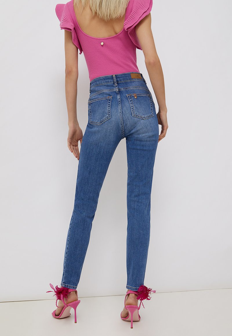 Jeans blu a vita alta con una forma aderente e tasche posteriori, abbinati a sandali con tacco rosa con accenti floreali.