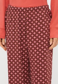 Bruine pyjamabroek met een geometrisch patroon in roze en lichtroze accenten. Ze hebben een elastische tailleband voor extra comfort.