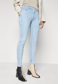 Vaqueros skinny de color azul claro con un ajuste clásico, que presentan una cintura de altura media y detalles de costura sutiles. Combinados con botas de tacón alto en dos tonos.