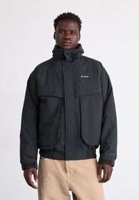 Schwarze wasserdichte Jacke mit hohem Kragen, zwei großen Fronttaschen, elastischen Bündchen und verstellbarem Saum. Mit Columbia-Logo.