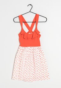 Robe sans manches avec un haut orange à volants, bretelles croisées, et jupe blanche ornée de pois orange, suspendue à un cintre noir.