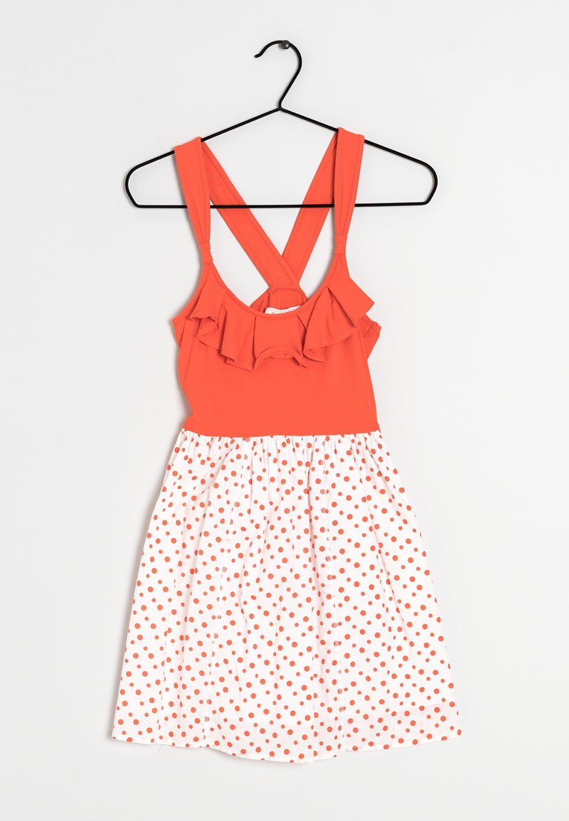 Robe sans manches avec un haut orange à volants, bretelles croisées, et jupe blanche ornée de pois orange, suspendue à un cintre noir.