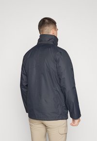 Navy waterproof jacket with high collar, adjustable cuffs, and a smooth texture; features a back yoke and seams for fit enhancement.