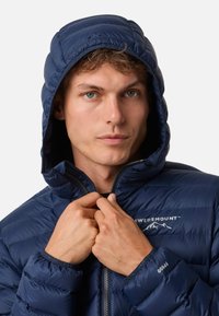 Navy pufferjack met een quilt-design, ritsluiting en capuchon. Beschikt over een logo op de borst en elastische manchetten voor een snug fit.
