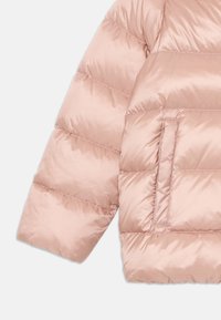 Manga e bolso lateral de um casaco puffer acolchoado rosa visíveis, com costura horizontal e textura de tecido brilhante e suave.