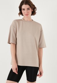 Beige oversized t-shirt med korte ærmer, rund halsudskæring og glat tekstur, parret med sorte cykelshorts.