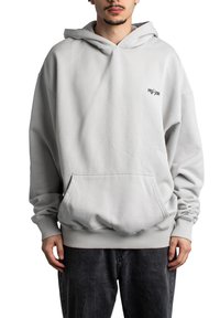 Lys grå oversized hettegenser med frontlomme, ribbede mansjetter og skjortekant. Har en liten svart logo på brystet, laget av mykt stoff.