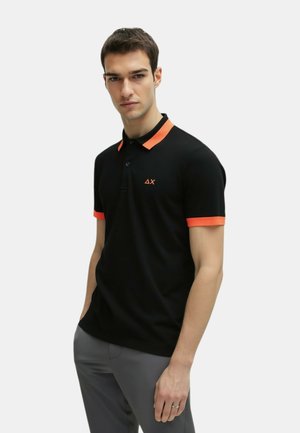 Polo nero con colletto e dettagli arancioni sulle maniche, dotato di un'apertura con tre bottoni e un piccolo logo sul petto. Tessuto dalla texture liscia.