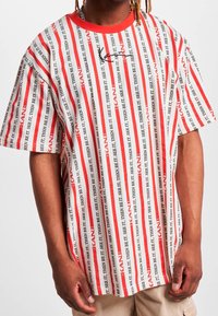 Camiseta de manga corta con rayas verticales rojas y blancas, con patrón de texto repetido en negro. Cuello redondo. Material de algodón.