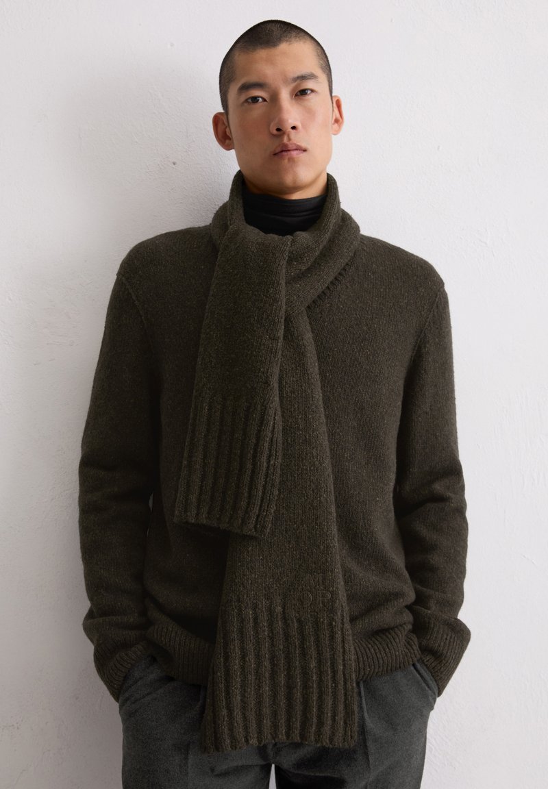 Maglione lavorato a maglia verde scuro con colletto alto, abbinato a una sciarpa a coste coordinata. Texture calda, design casual, dettagli di cucitura visibili sugli indumenti.