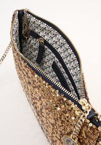 Kultainen paljettilaukku vetoketjulla. Sisällä on kuvioitu vuori valkoisena ja laivastonsinisenä, kaksi taskua ja kultainen lukko ketjuhihnaa varten.