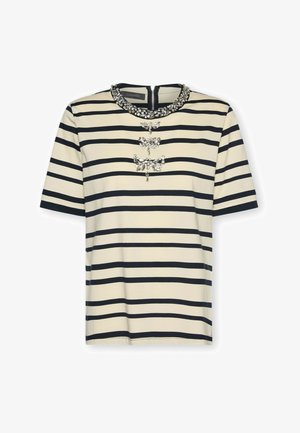 Kremowo-czarna, poziomo prążkowana bluzka z krótkim rękawem, okrągłym dekoltem ozdobionym kamieniami szlachetnymi oraz trzema dekoracyjnymi kokardami wysadzanymi kamieniami na piersi.