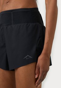 Czarne sportowe spodenki o gładkiej teksturze, z logo Nike na dolnej lewej stronie i zabezpieczonym pasem.