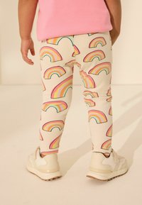 Medvilninės leggings, turinčios kreminį pagrindą su daugiaspalvėmis vaivorykštės raštais. Suderintos su béže spalvos sportiniu apavu, jos turi tvirtą prigludimą ir lygų paviršių.