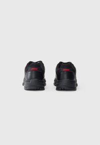 Black sneakers with mesh and synthetic material, featuring a textured sole, padded collar, and red logo accents on the heel.