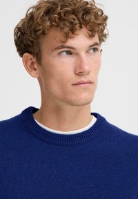 Niebieski sweter z okrągłym dekoltem wykonany z dzianiny, z prążkowanym kołnierzem i mankietami. Miękka tekstura w jednolitym kolorze, bez widocznych wzorów.