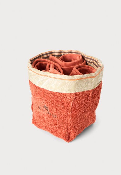 Panier en tissu orange à texture douce avec une serviette roulée à l'intérieur, présentant une bordure beige à motifs et un détail brodé sur le côté.