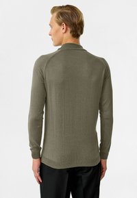 Khaki lange mouw sweater met ronde hals, geribde manchetten en zoom. Soepele textuur en aansluitend ontwerp, gezien vanuit de achterkant.