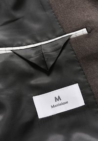Brown fabric interior with a smooth black lining. Includes a small pocket with a white lining and a tag displaying "Matinique."