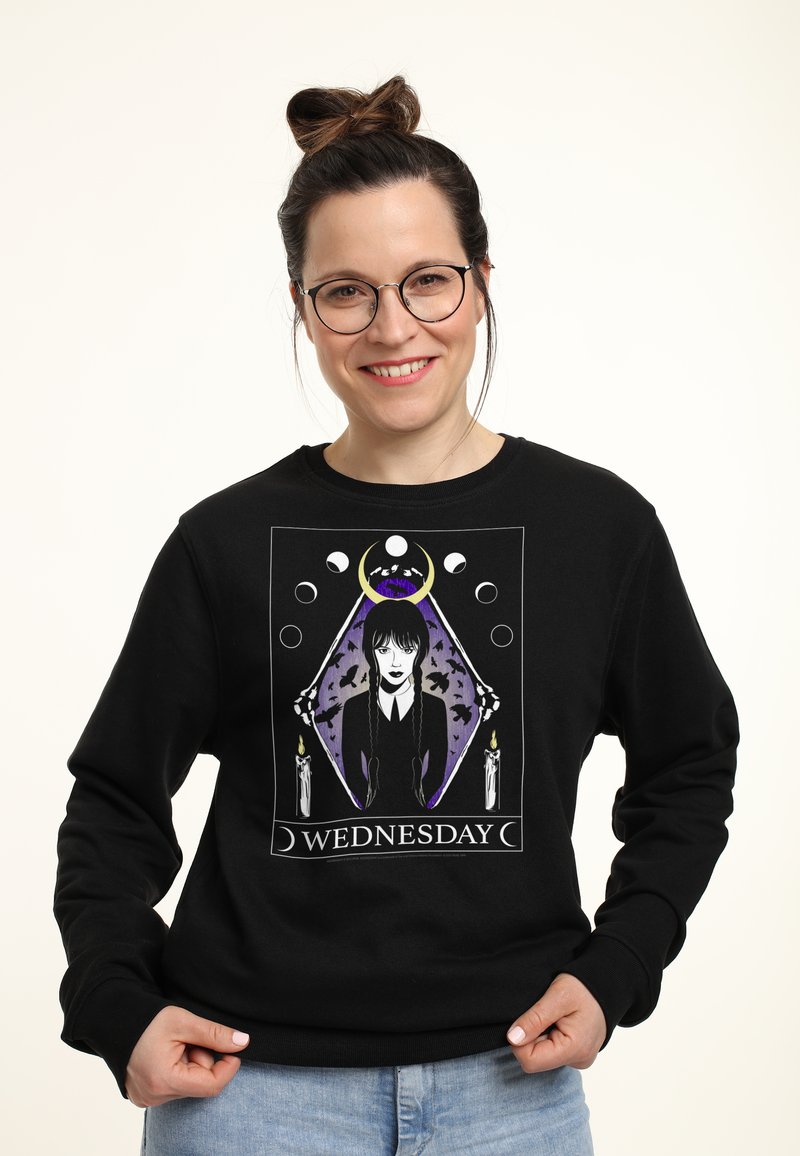 Felpa nera con una grafica di un personaggio con capelli lunghi davanti a un diamante viola, affiancato da candele e la scritta "WEDNESDAY."