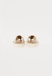 Sandale plate cu un superior din fibră naturală împletită, de culoare bej, și o talpă platformă texturată albă. Design simplu, cu spatele deschis.