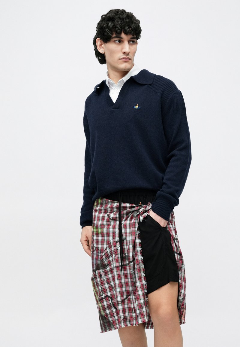 Marineblå strikket sweater med v-hals og ribbede manchetter, kombineret med et ternet omslagsskjørt med røde, grønne og hvide farver samt en sort panel.