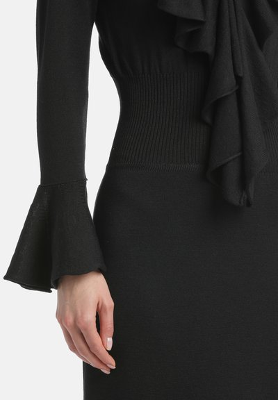Czarna dzianinowa sukienka z falbaniastymi akcentami przy dekolcie oraz szerokimi mankietami. W talii znajduje się prążkowany, teksturowany pas, który dodaje charakteru.