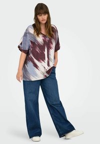Chemise ample à manches courtes ornée d'un imprimé abstrait multicolore dans des teintes bourgogne et bleues, associée à un jean en denim à jambe large.