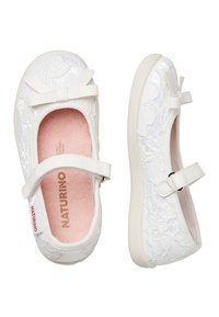 Ballerine bianche con un design in pizzo testurizzato, dotate di un piccolo fiocco sulla parte anteriore e di una chiusura con strap in Velcro. Soletta rosa e suola flessibile.