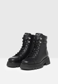 Black leather ankle boots with a rounded toe, lace-up front, zip closure, chunky sole, and decorative white stitching along the base.