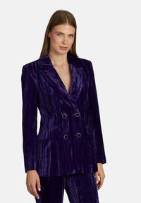Blazer doppiopetto in velluto viola con rever affilati, due tasche e dettagli metallici. Finitura texturizzata, vestibilità su misura.