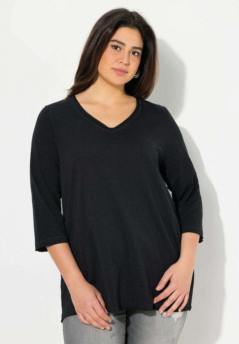 Musta V-päinen paita, jossa on kolme neljännestä hihoista, pehmeä kangas ja kaareva helma. Ominaisuuksiin kuuluu yksinkertainen ompelutaito kaula-aukossa.