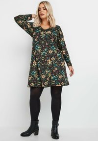 Pitkähihainen mekko, jossa on kukkakuosi keltaisen, sinisen ja punaisen sävyissä mustalla taustalla. Ominaisuuksiin kuuluu V-pääntie ja leveä alaosa.