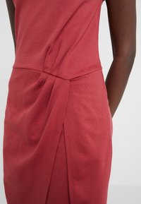 Vestido rojo sin mangas con textura lisa, que presenta detalles de tela fruncida en la cintura y una silueta ajustada.