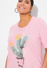 Top corta de manga corta en color rosa con un gráfico de cactus, flores amarillas y el texto "NO ME TOQUES", confeccionado en una tela suave y ligera.