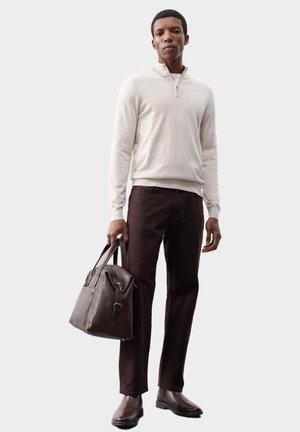 Maglione zip-up grigio chiaro, pantaloni marroni e borsa in pelle marrone scuro. Il modello indossa scarpe marroni; l'outfit presenta un design minimalista.