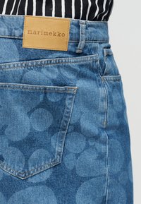 Τζιν φούστα με κυκλικό σχέδιο, πίσω τσέπη, ετικέτα από ταμπά δέρμα Marimekko, φορεμένη με μαύρο-λευκό ριγέ τοπ που φαίνεται στη μέση.